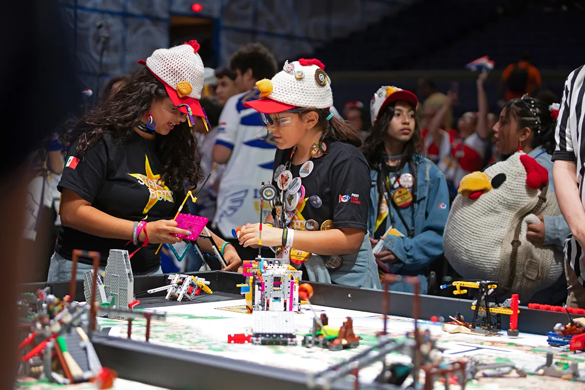 Deelnemers aan de FIRST LEGO League werken samen aan een LEGO-robot bij de wedstrijdtafel.